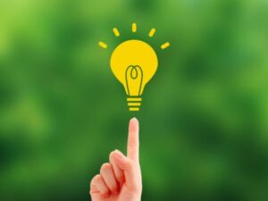 緑背景に指先で触れる黄色い電球